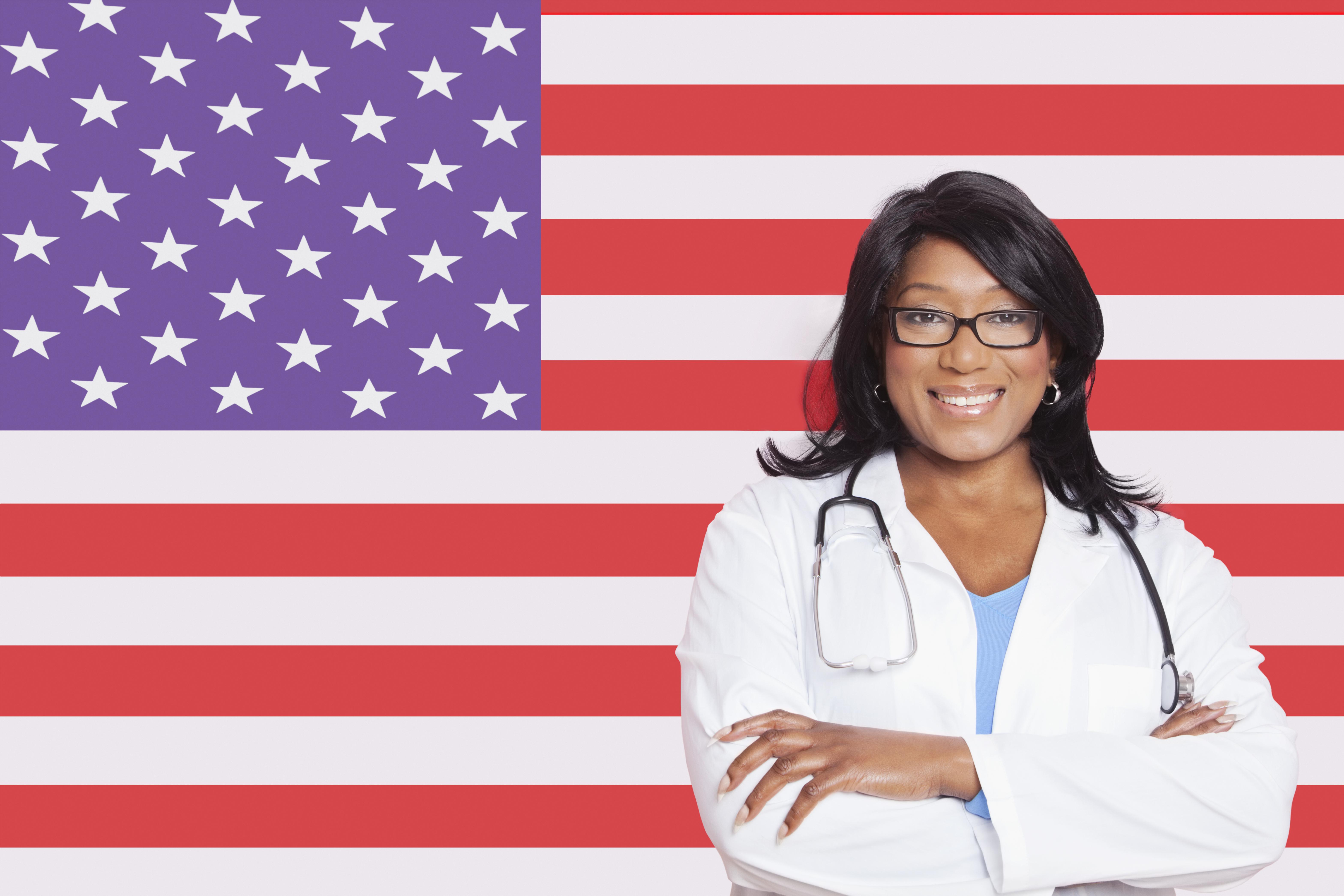 Portrait of confident mixed race female surgeon over American flag