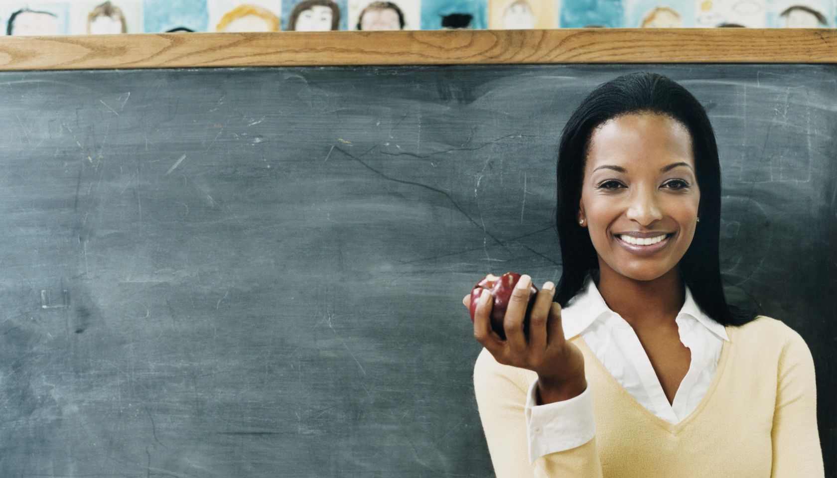 Portrait of a Teacher Standing in Front of a Blackboard Eating an Apple