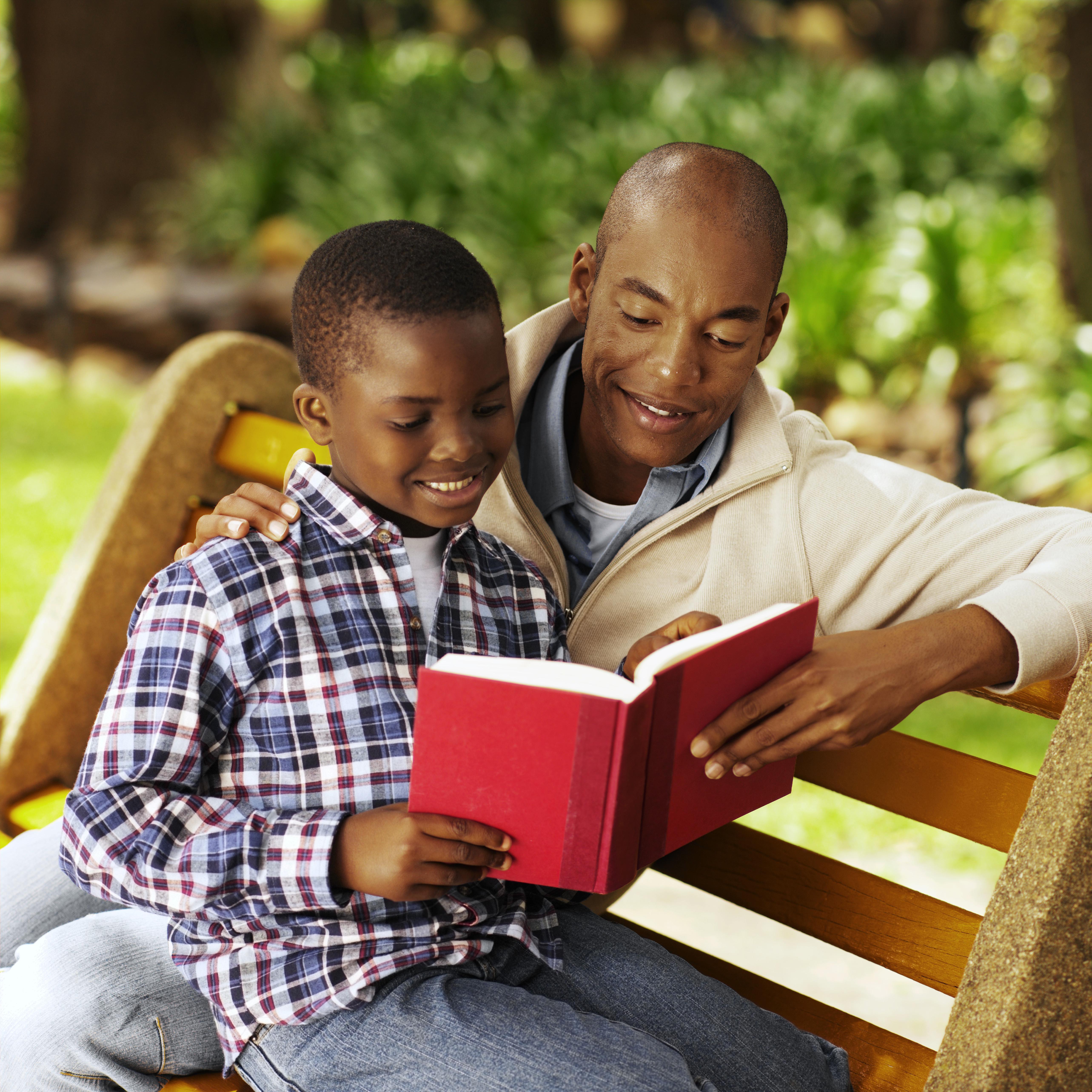 Close-up of father and son sitting on bench reading book (10-11)