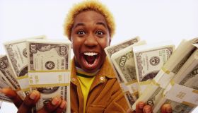 Young man holding bundles of US dollars, smiling, portrait