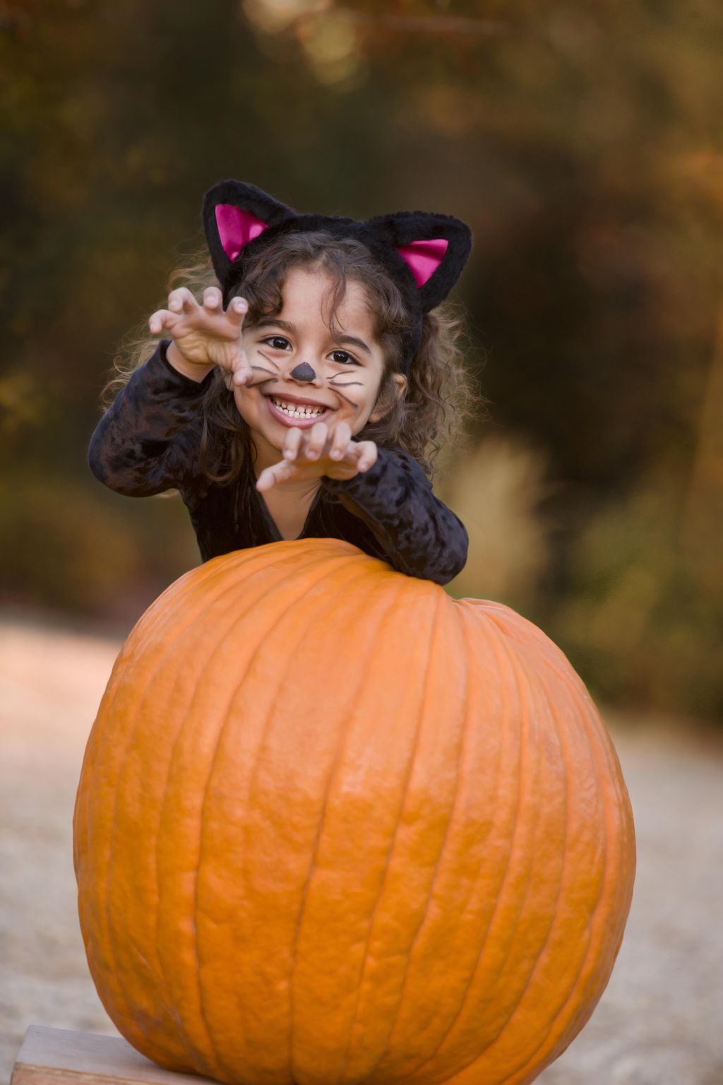 Girl (4-5) in cat costume standing behind pumpkin, portrait