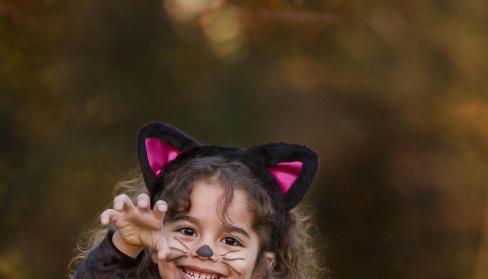 Girl (4-5) in cat costume standing behind pumpkin, portrait