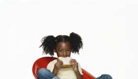 Girl (6-7) sitting on chair, eating peanut butter sandwich, portrait