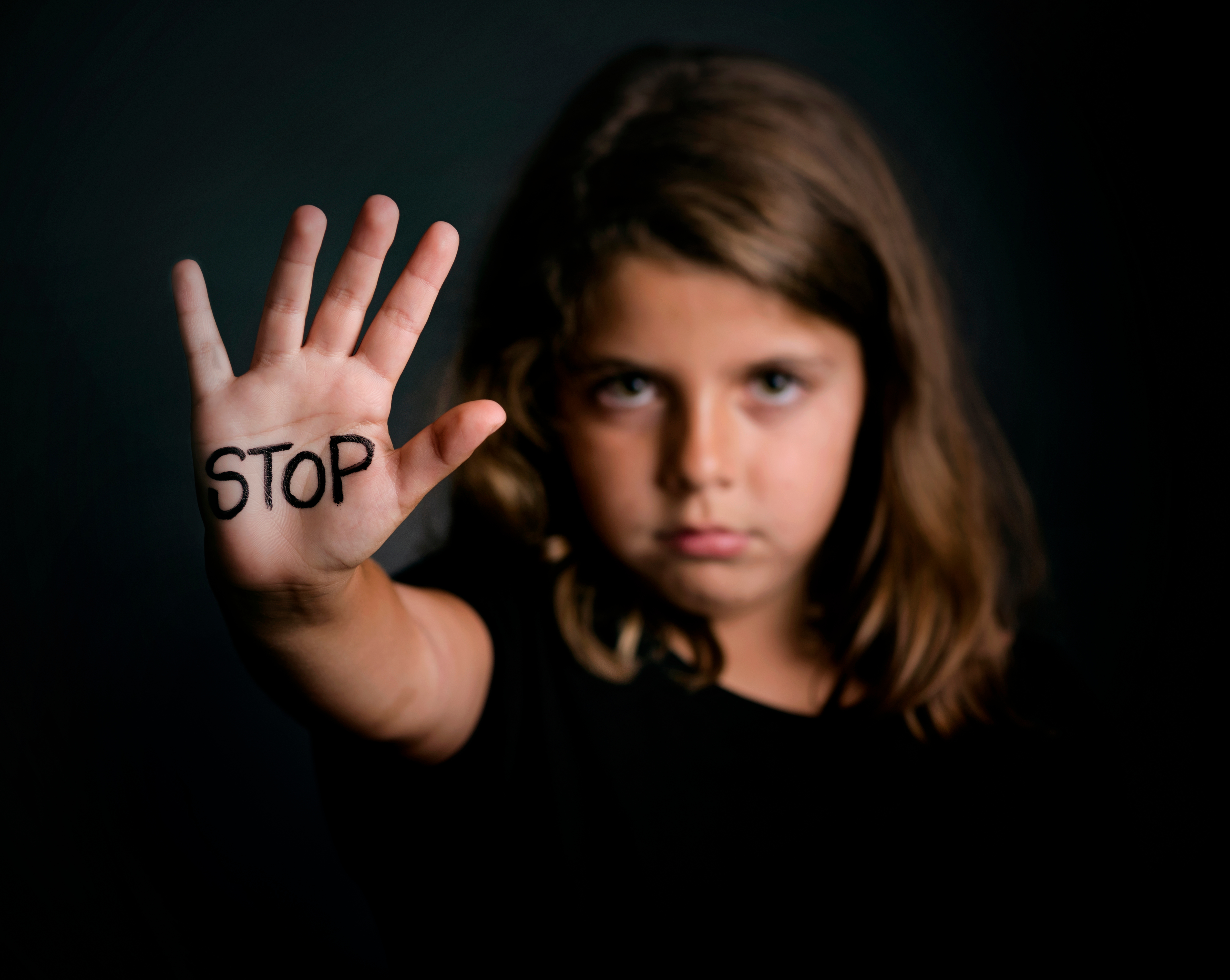 Close-Up Of Girl Showing Stop Text On Palm Against Black Background