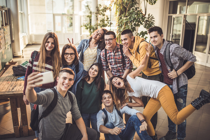 Large group of happy students taking a selfie with cell phone at school.