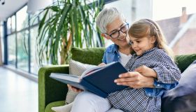 Grandmother sitting on couch with granddaughter, reading book together