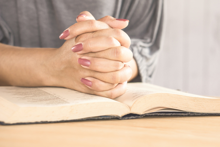 Cropped Image Of Woman With Hands Clasped And Book On Table