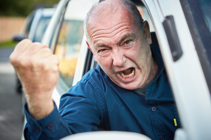 Road rage: furious senior male driver shaking fist and shouting