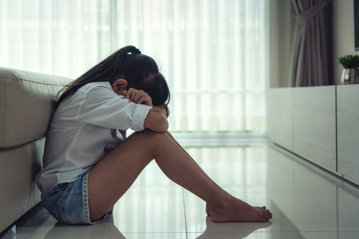 Depressed Asian little girls sitting on the floor hugging her knees in sad moody at home. She feel lonely and sadness.