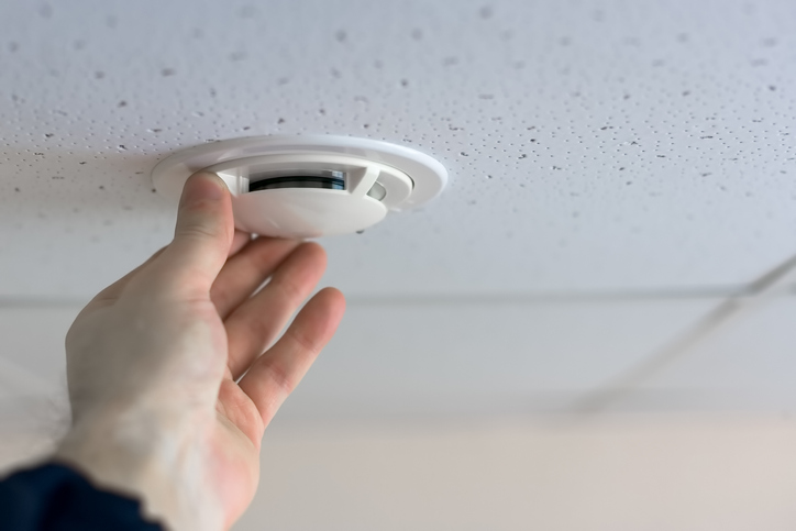 Cropped Hand Adjusting Smoke Detector On Ceiling