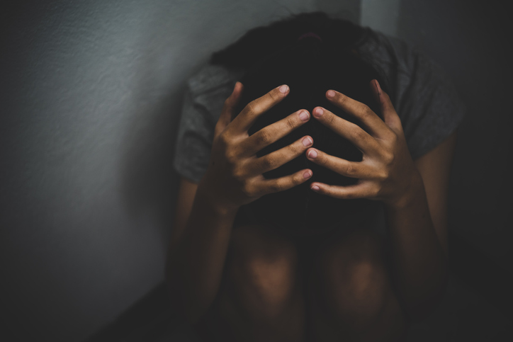 High Angle View Of Sad Girl Covering Face While Sitting Against Wall