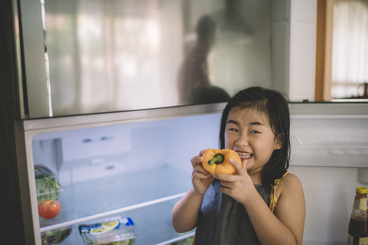 an asian chinese child took out yellow bell pepper from refrigerator and have a bite on it