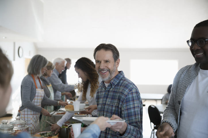 Smiling man serving food at soup kitchen community dinner