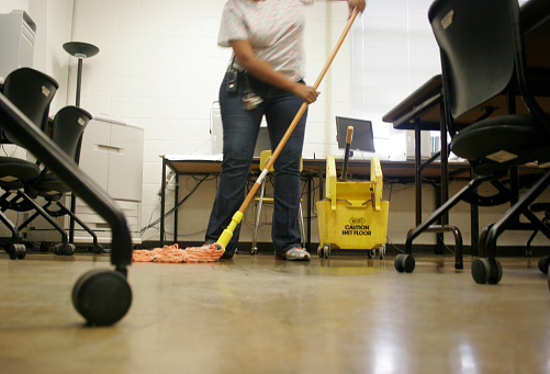 A female janitor sweeps the floor with a broom and dustpan in a historic shopping mall, (low angle).