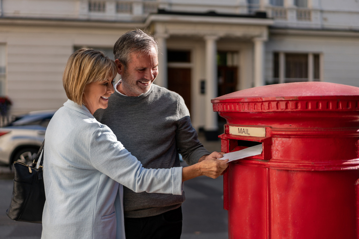 Happy adult couple putting a letter in the mail