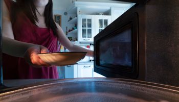 Young woman introducing plate in microwave oven view from inside