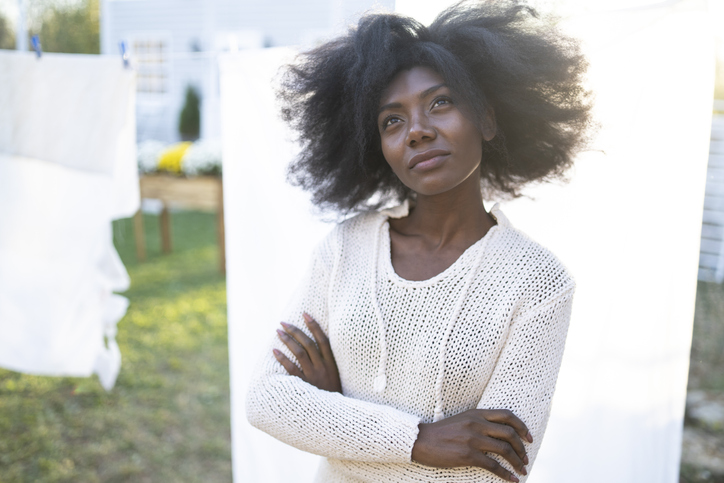 African woman in casual white clothes standing arms crossed in back yard