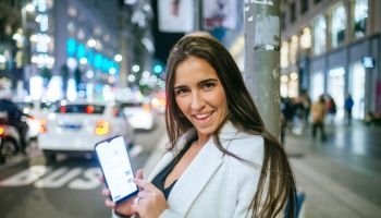 Happy woman showing her smartphone in the street at night