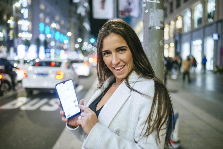 Happy woman showing her smartphone in the street at night