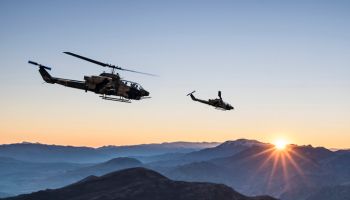 AH-1 Cobra Attack helicopters flying over mountains at sunrise