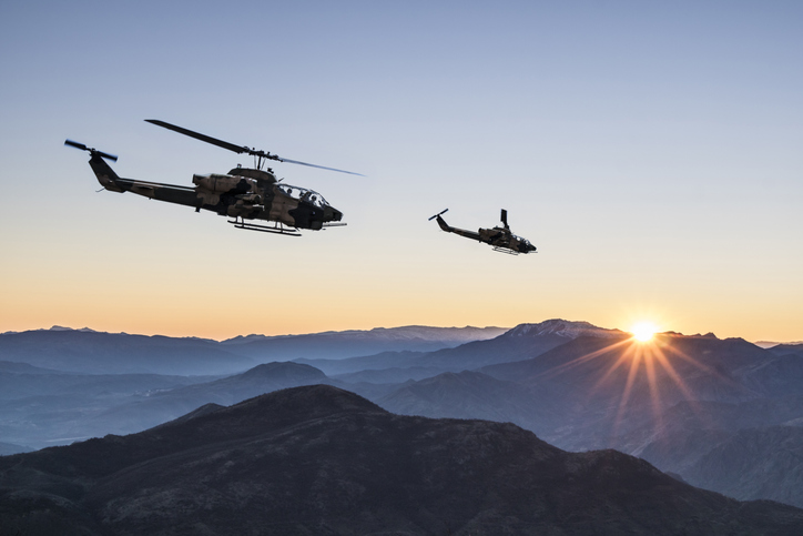 AH-1 Cobra Attack helicopters flying over mountains at sunrise