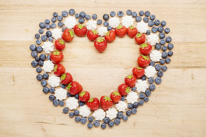 High angle view of strawberries, blueberries and meringue arranged in heart shape on wooden table