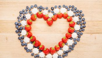 High angle view of strawberries, blueberries and meringue arranged in heart shape on wooden table