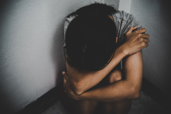 High Angle View Of Sad Girl Covering Face While Sitting Against Wall