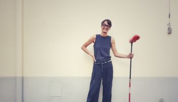 Portrait Of Smiling Woman Holding Broom While Standing Against Wall