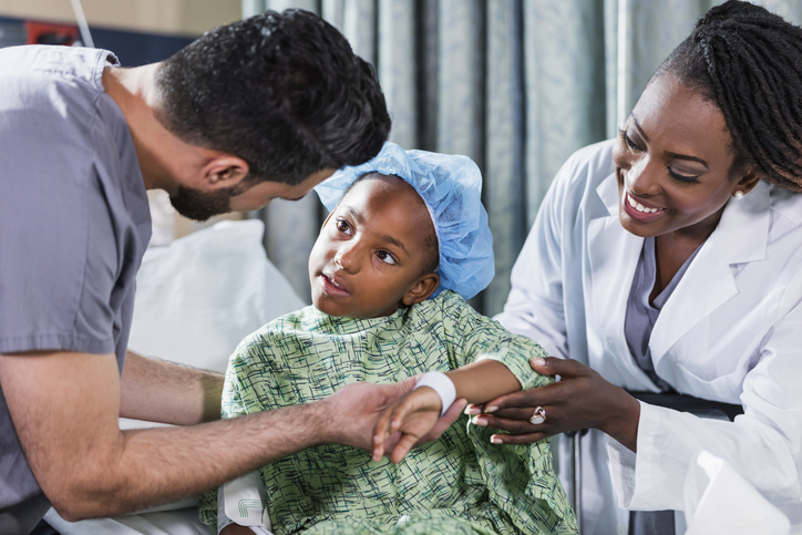 Doctor, nurse helping girl sitting on hospital bed