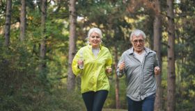 Beautiful senior couple running outside in sunny autumn forest