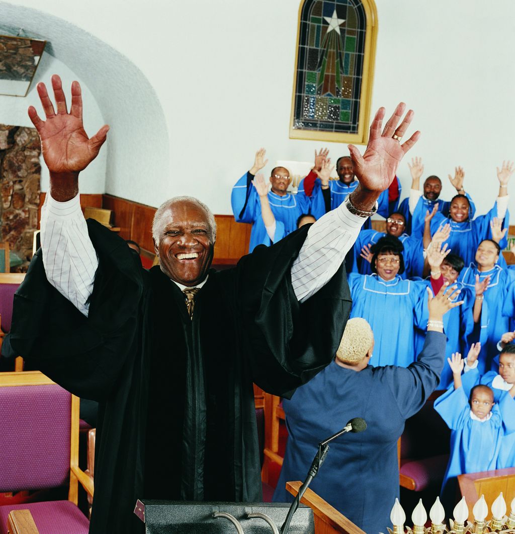 Priest Standing on a Pulpit With His Arms Upraised in Front of a Gospel Singing Choir
