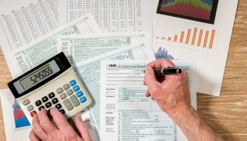 Cropped Hands Of Man Filing Documents Using Calculator At Table