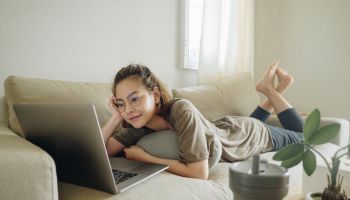 Teenager woman lying on sofa and using social network at home.