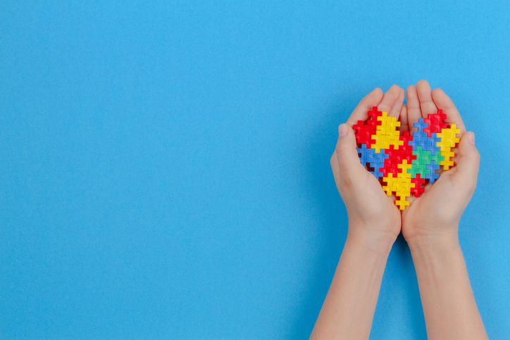 Kid Hand Holding Colorful Heart On Blue Background. World Autism Awareness Day Concept.